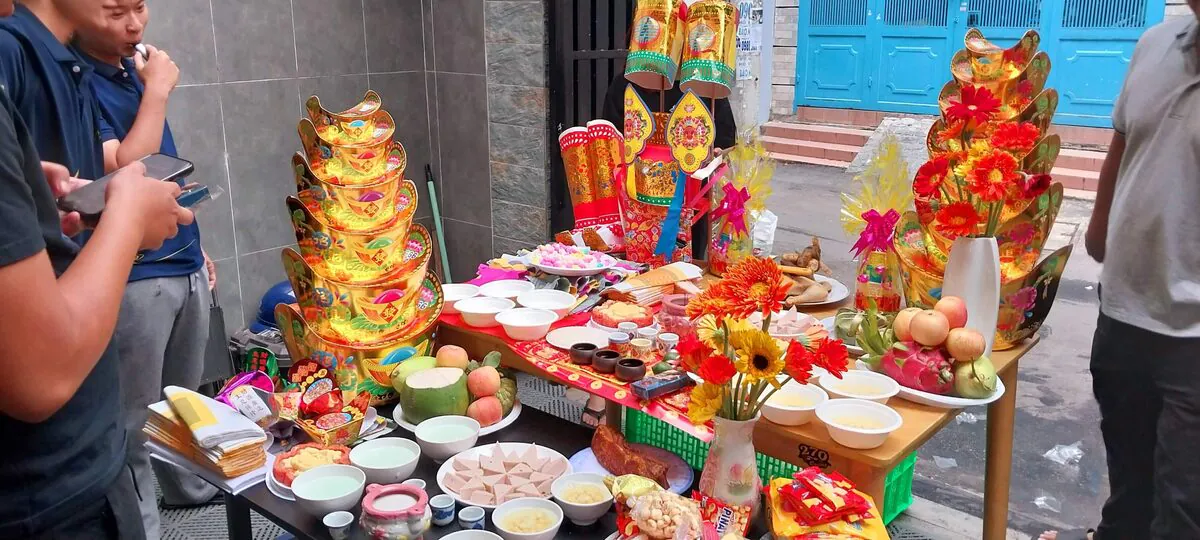 Mâm cúng cô hồn và quan thần linh bày ngoài trời gồm miếng thịt heo quay, đĩa chả lụa cắt tam giác, gà luộc, 12 chén cháo chè, dừa tươi, hai tháp vàng mã và bộ mũ áo ủng giấy
