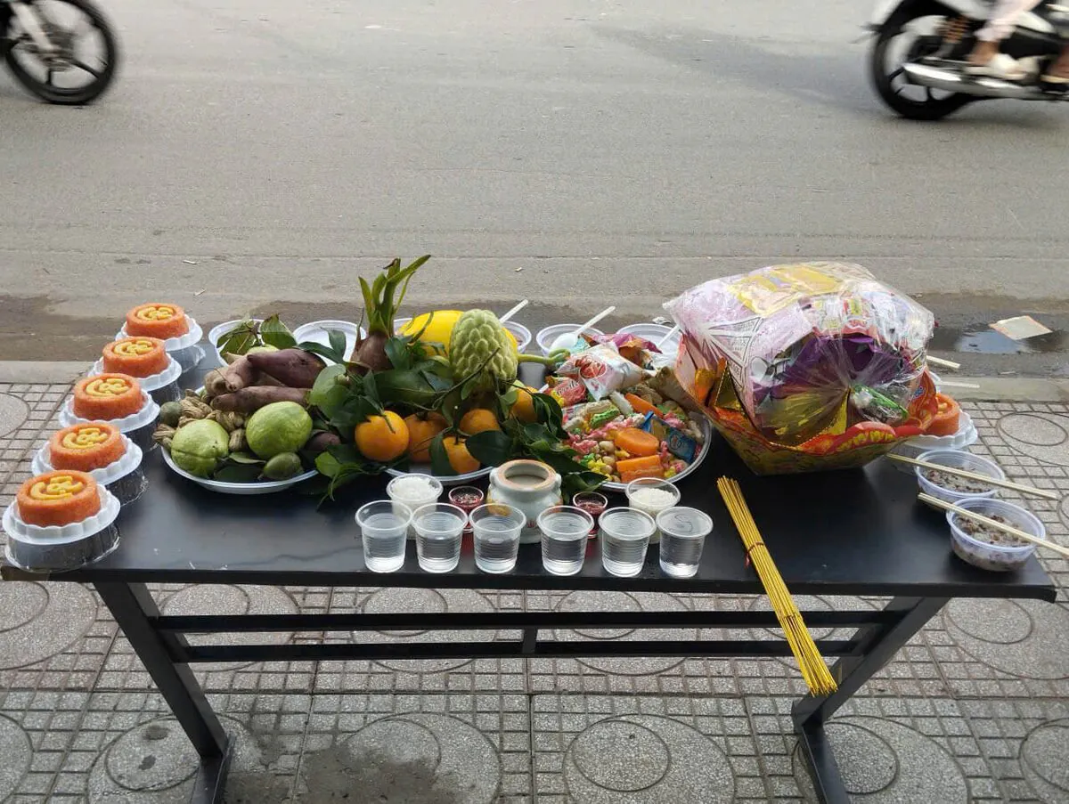 Mâm lễ cúng cô hồn chay hàng tháng đặt ngoài vỉa hè với 6 đĩa xôi gấc chữ Lộc, cháo trắng, chè, đĩa khoai lang luộc đậu phộng ổi xanh, mâm trái cây tươi, bánh kẹo và lễ vật giấy tiền