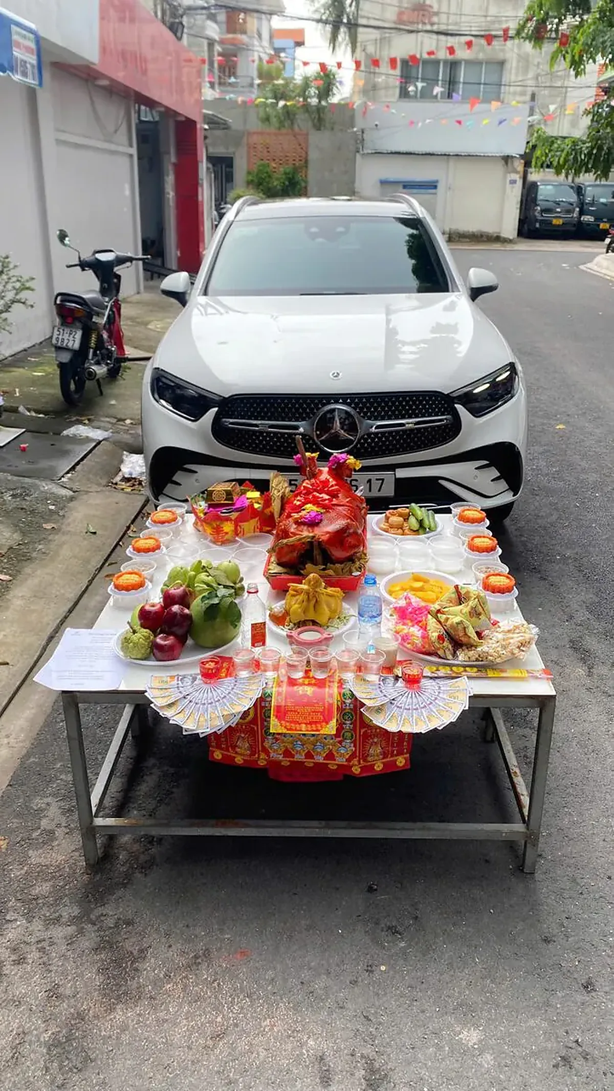 Mâm Cúng Xe Ô Tô Mới Mercedes-Benz GLC Màu Trắng Với Heo Sữa Quay & Gà Trống Luộc Mâm cúng xe mới đặt ngay trước mũi xe SUV Mercedes-Benz GLC màu trắng gồm heo sữa quay nguyên con, gà trống luộc, 6 đĩa xôi gấc chữ Lộc, bánh phu thê, ngũ quả và tiền giấy xếp hình quạt — Mâm Cúng Xe Cần Những
